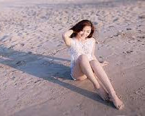 Woman sitting on a sandy beach with a long shadow